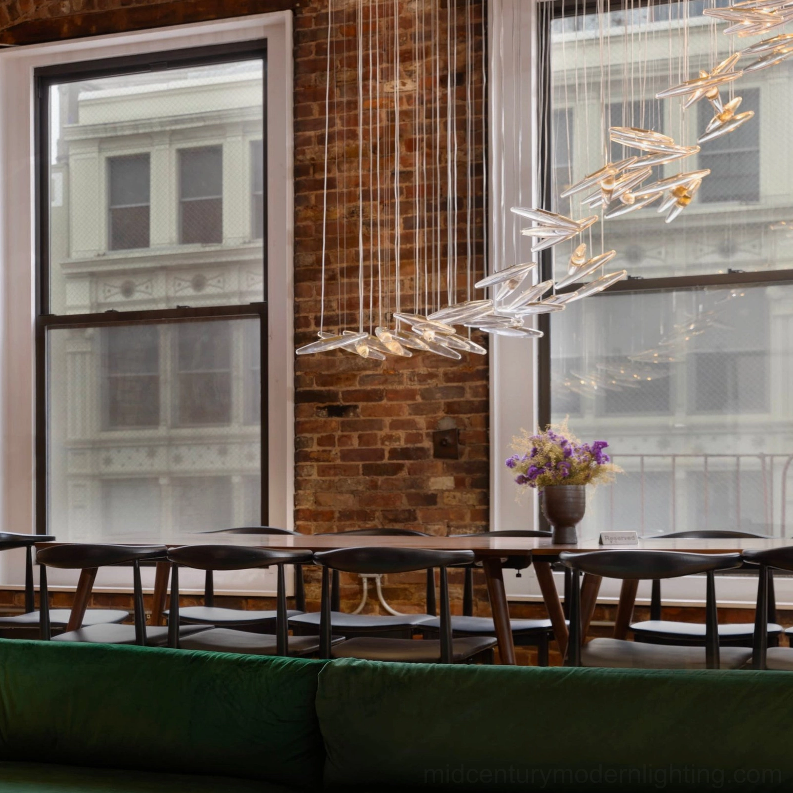 Dual-tone leaf glass chandelier in loft-style dining space with green velvet sofa and dark wood table