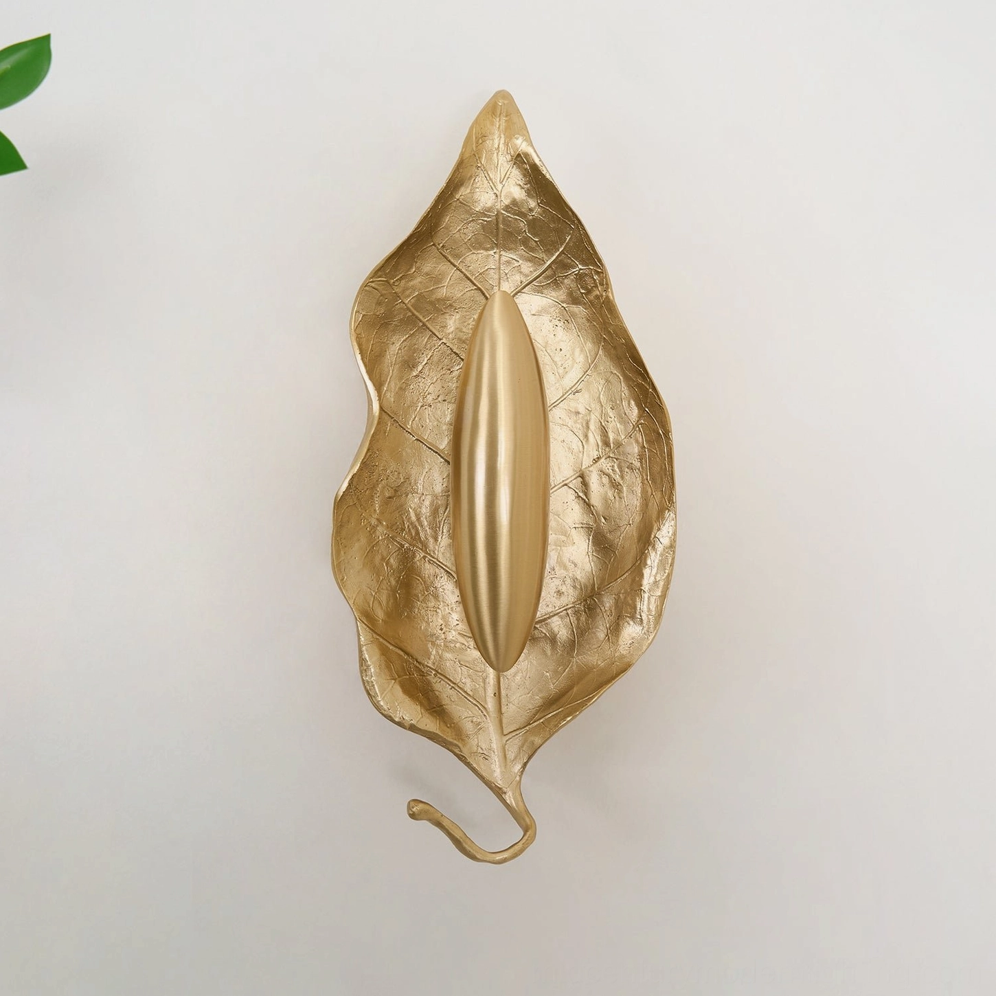 Full frontal view of Dumaine brass leaf wall sconce with smooth gilded finish and curled leaf tail against studio background