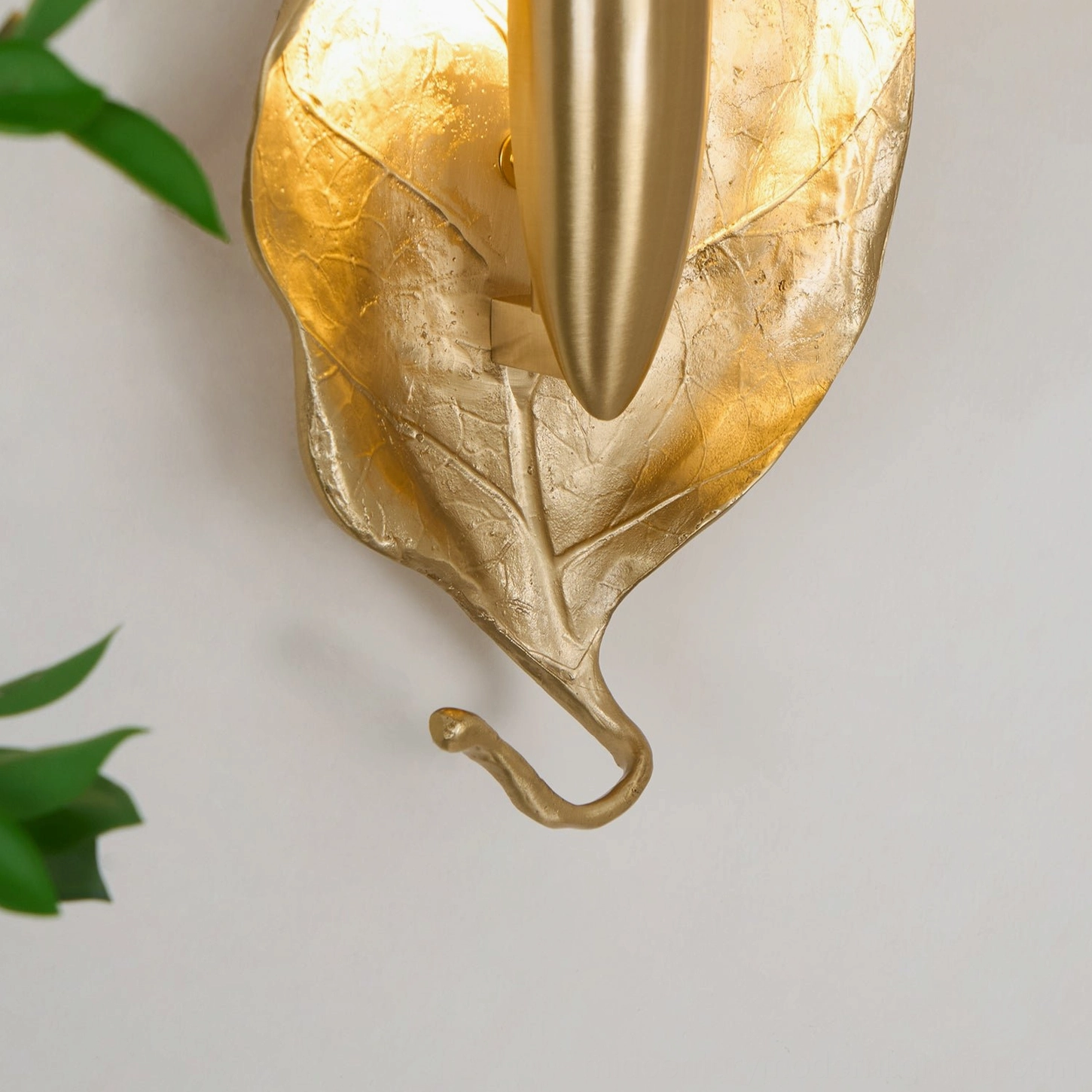 Close-up extreme detail of Dumaine wall sconce showing polished brass fixture, leaf veins, and light diffusion