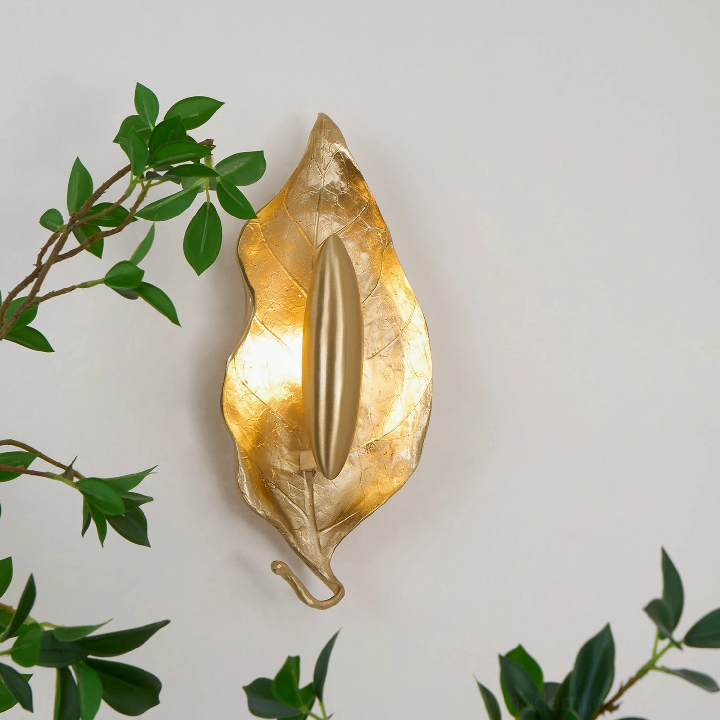 Illuminated Dumaine leaf wall lamp mounted on white wall with green foliage styling, three-quarter angle showing warm ambient glow