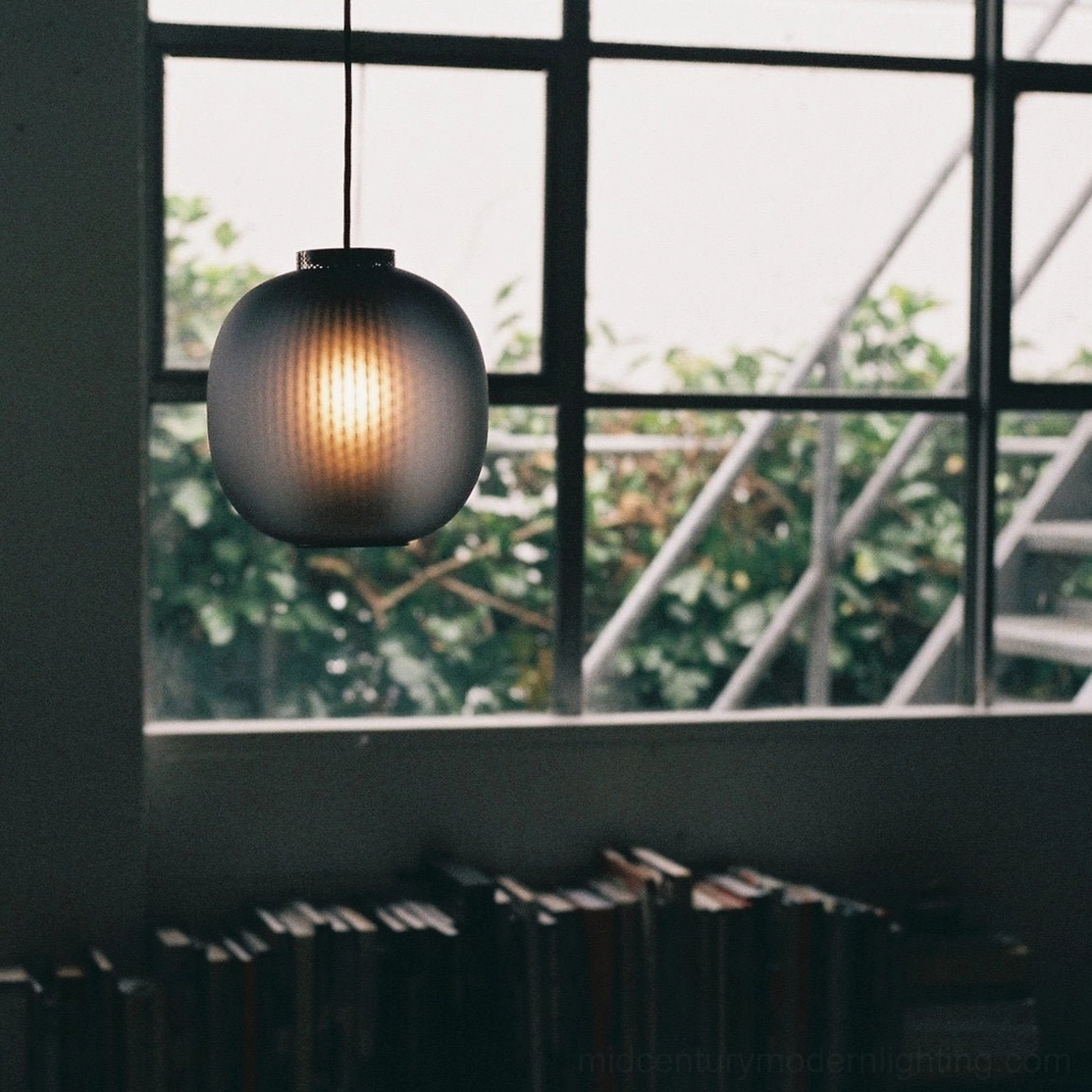 Single dark ribbed glass pendant light by bookshelf window with outdoor greenery