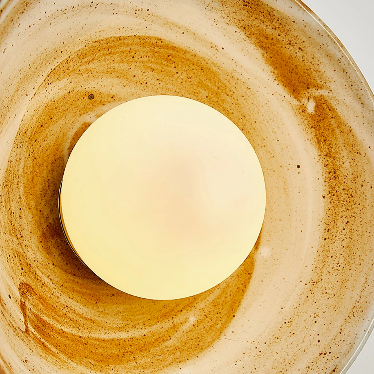 Eala wall lamp close-up detail of glowing frosted bulb with swirling brown ceramic shade texture