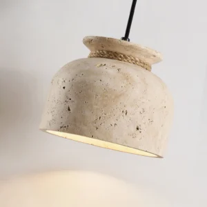 Easton natural stone pendant lamp lit from below, showing warm downlight and porous travertine detail against gray wall