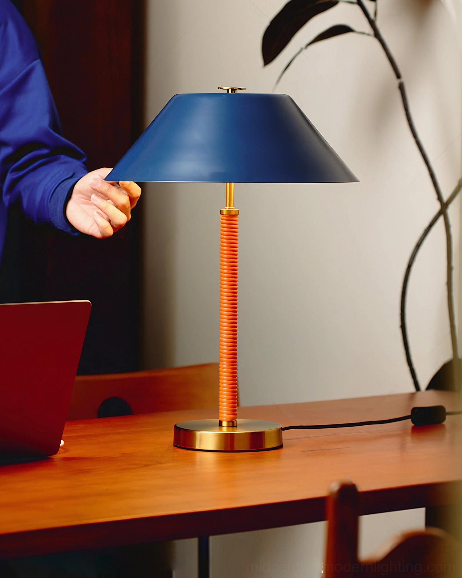 Eave modern table lamp in home office workspace on wooden desk with laptop, navy blue shade and corrugated orange stem