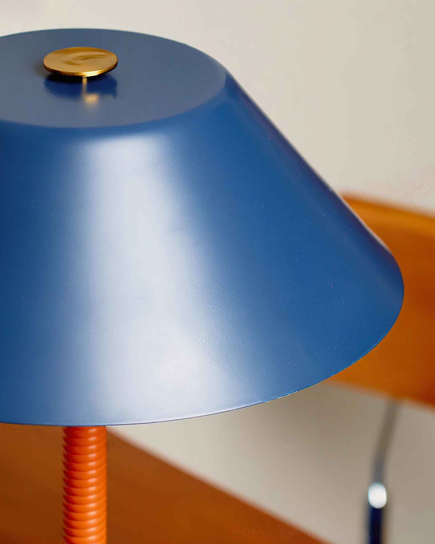 Eave table lamp shade and stem close-up detail shot, matte navy blue metal shade with brass finial and orange ribbed stem
