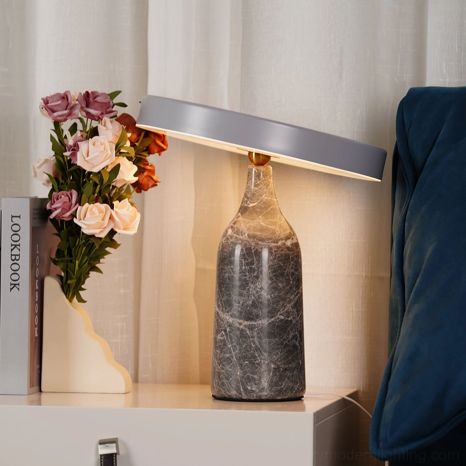 Eddy rotating marble lamp with grey shade displayed on indoor cabinet with flower vase and books