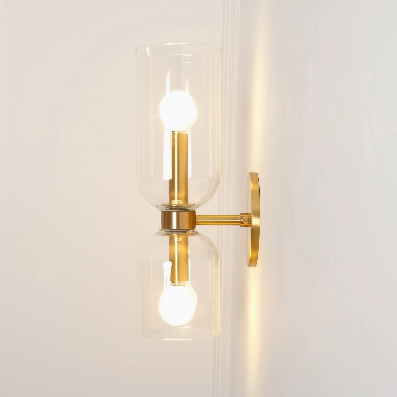 Contemporary glass wall lamp featuring clear transparent shade with brass frame and glowing Edison bulbs