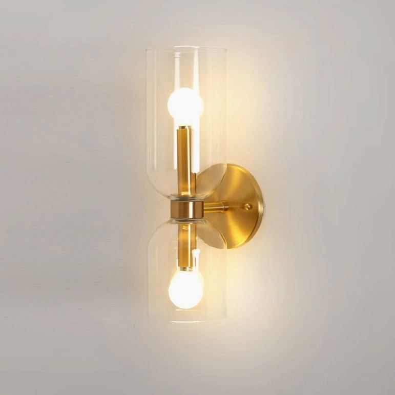 Mid-century modern wall sconce with transparent glass vessel and warm brass gold base mounted on white wall