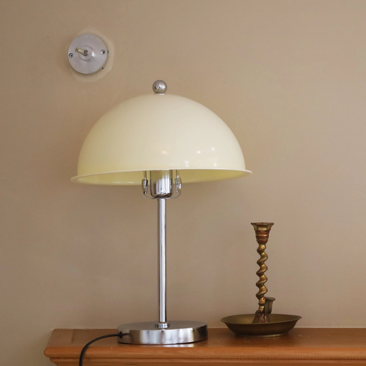 Edinburgh table lamp with beige shade on bedside table, eye-level frontal view with polished chrome base