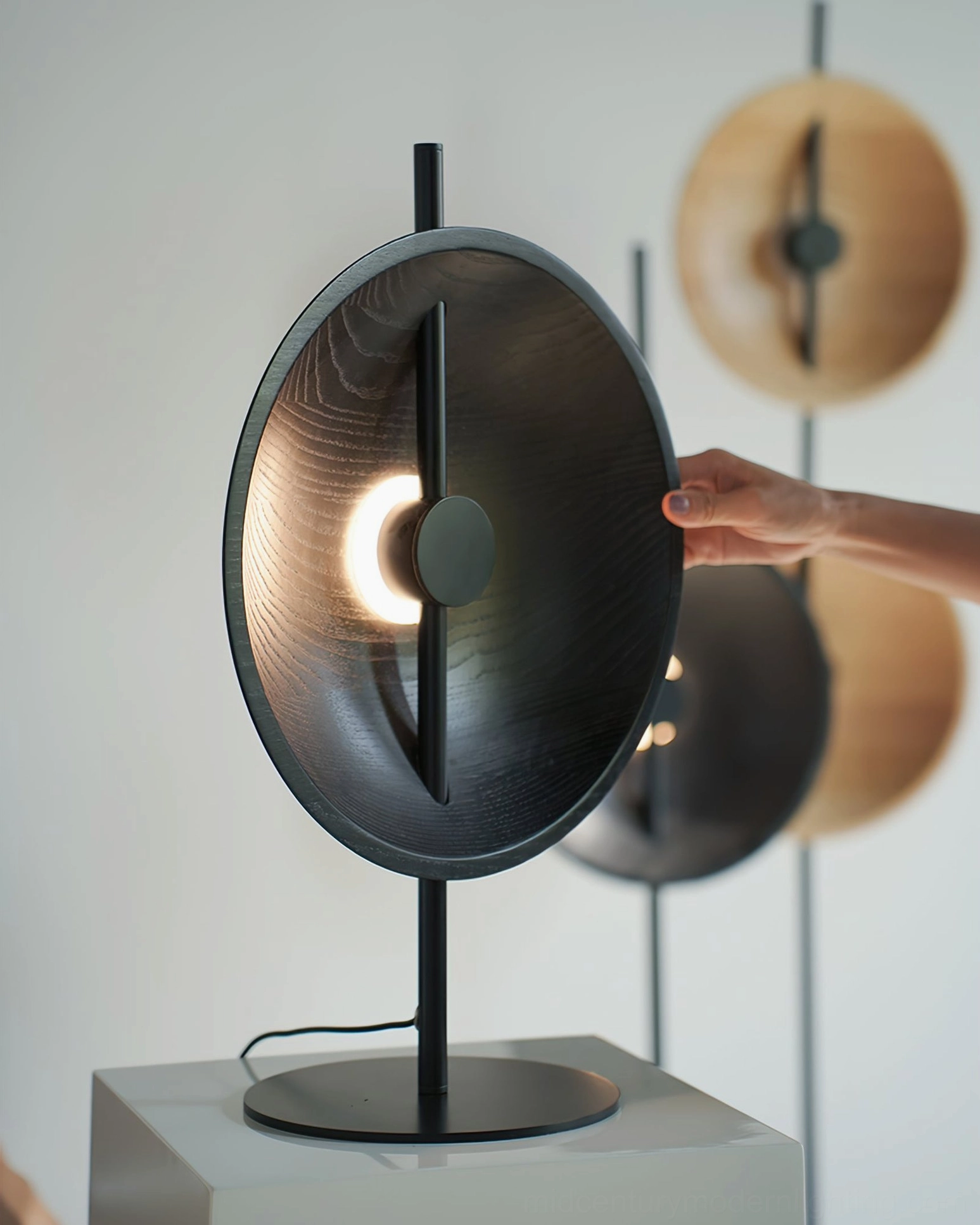 Eine matte black disc lamp three-quarter close-up view with hand model, showing texture and design details of mid-century modern lighting