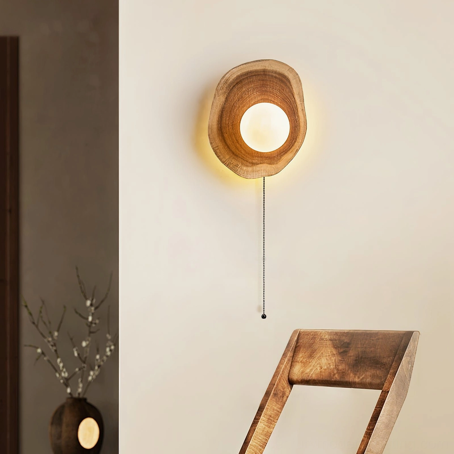 Eivor wood wall light installed in residential entryway with wooden chair and decorative vase, demonstrating warm ambient lighting in interior design context
