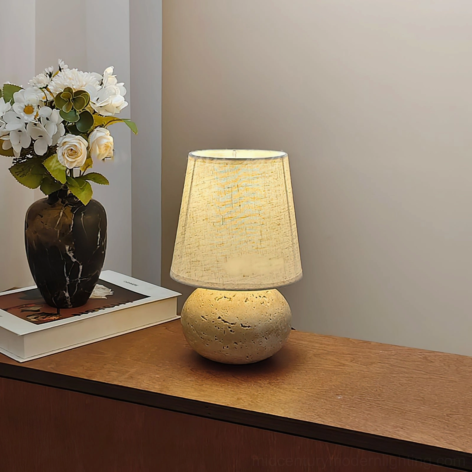 Unlit Elba table lamp right three-quarter view on wooden bedside table, travertine spherical base with simple linen shade and minimalist decor