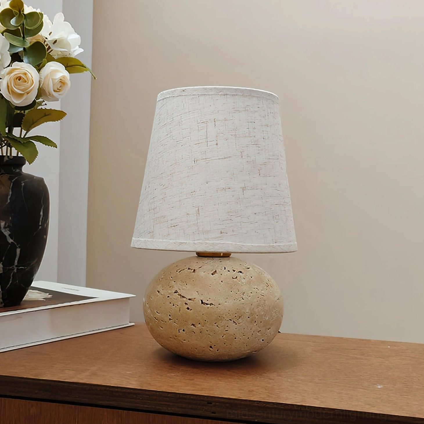 Front view of unlit Elba table lamp on wooden bedside table, solid white linen shade with travertine spherical base mid-century modern design