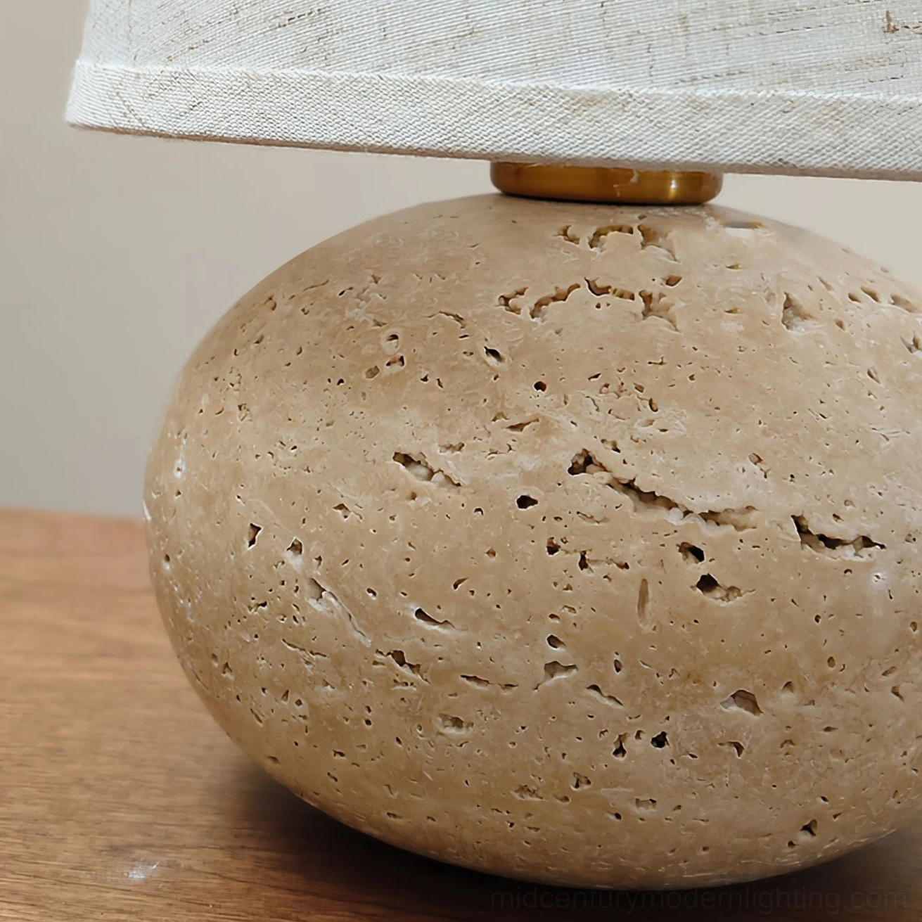 Macro close-up of Elba travertine table lamp base on wooden tabletop, showing natural porous stone texture and gold metal shade connector