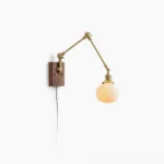 Elia swing arm wall lamp front view with frosted glass shade, brass arms, and walnut wood base on white background