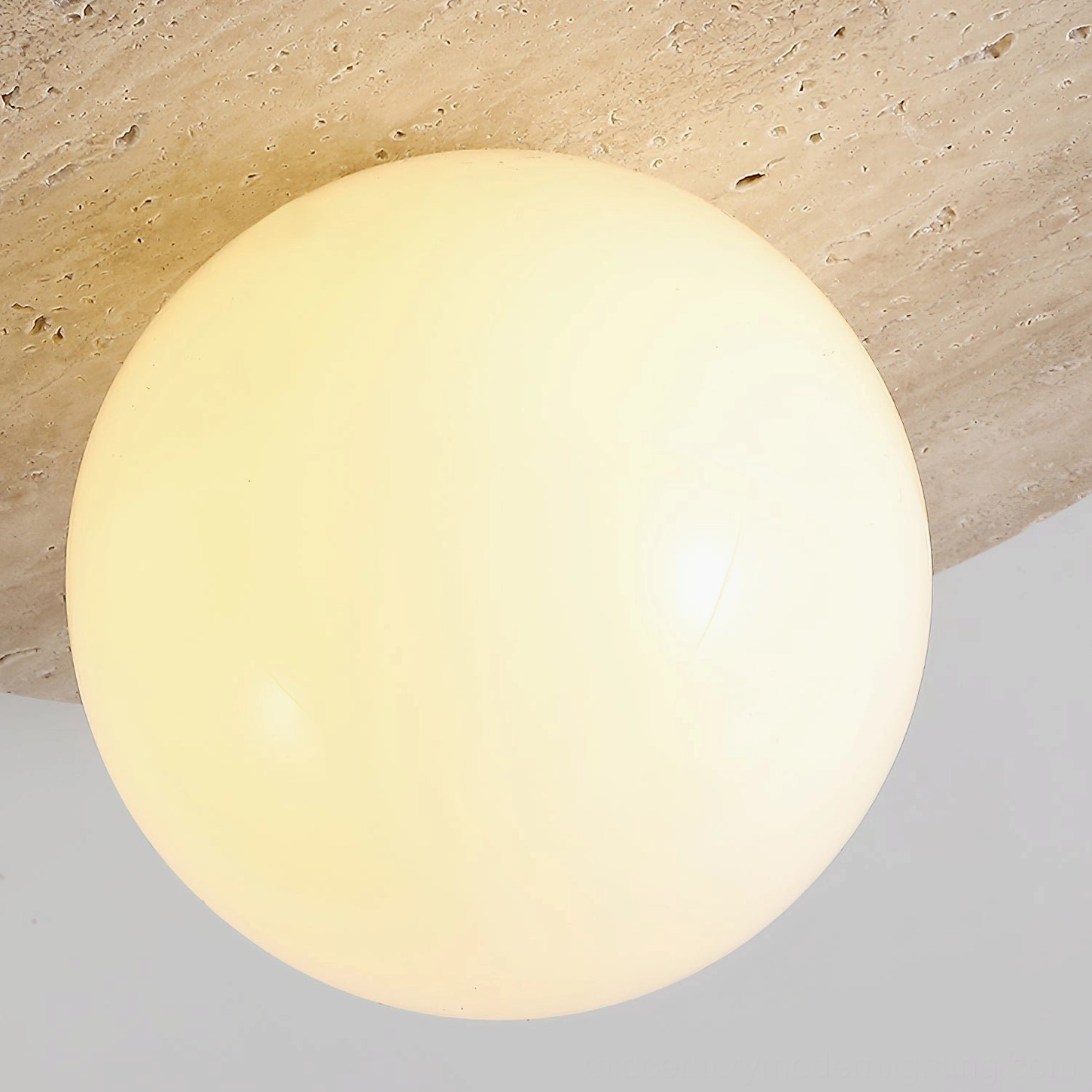 Travertine wall light fixture with spherical glass element, architectural lighting design detail shot