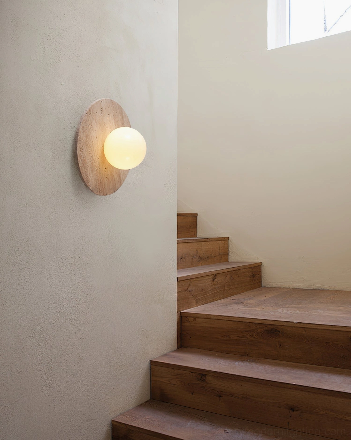 Travertine sphere wall lamp mounted on stucco wall near indoor staircase, architectural lighting application