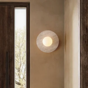 Travertine wall lamp mounted in minimalist entryway with wooden door, warm neutral lighting demonstration