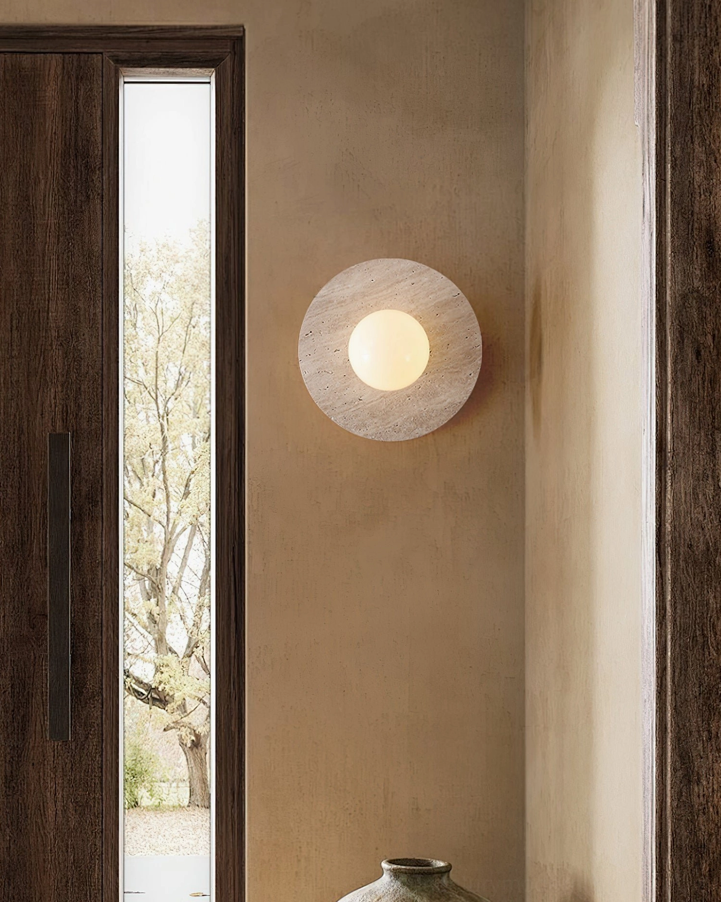 Elira travertine wall lamp in residential entryway showing side profile and warm ambient glow effect