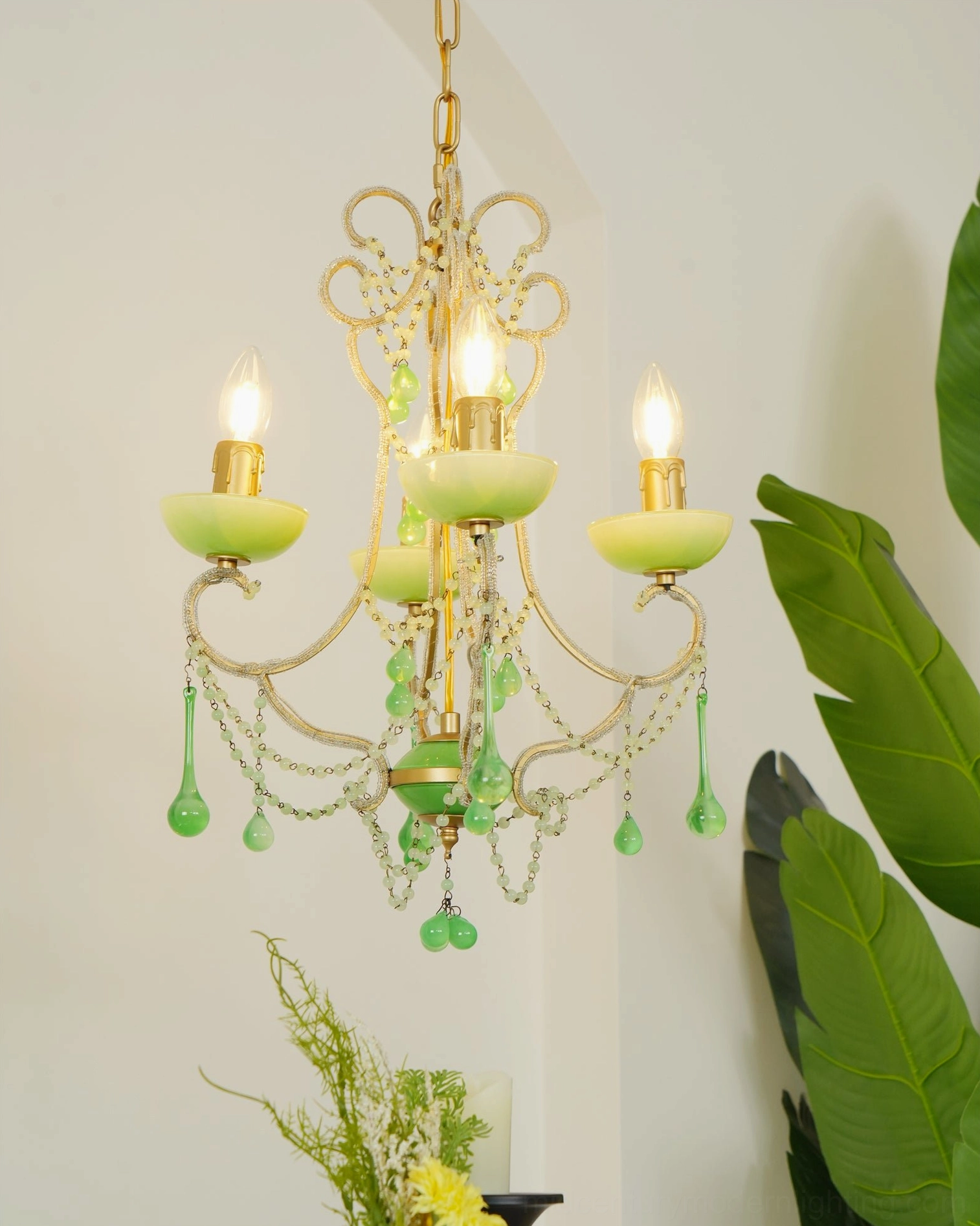 Compact emerald glass chandelier displayed in corner with tropical potted plants and green glass drop pendants