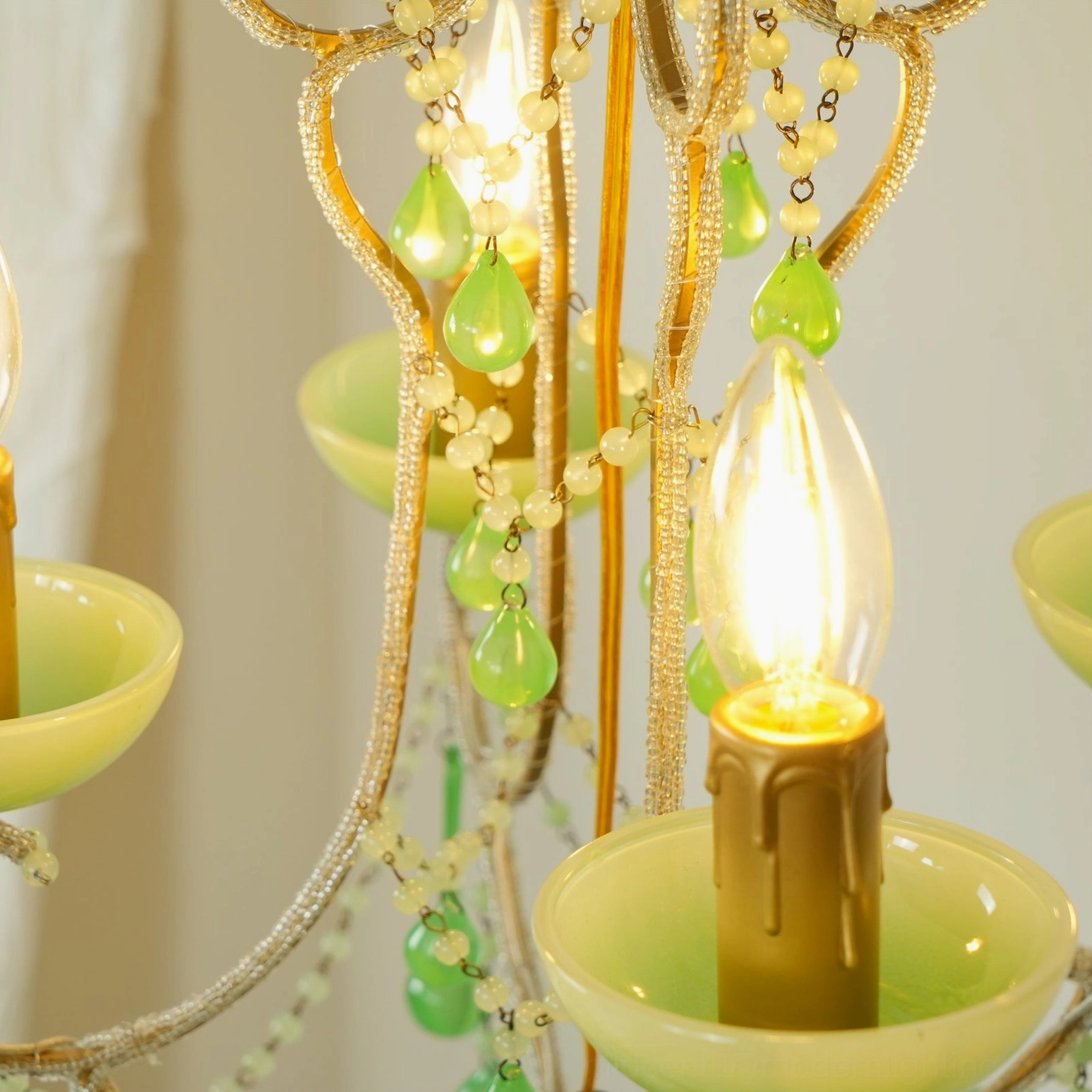 Extreme close-up detail of emerald green Murano chandelier showing glowing bulb, beaded chains, and gold frame