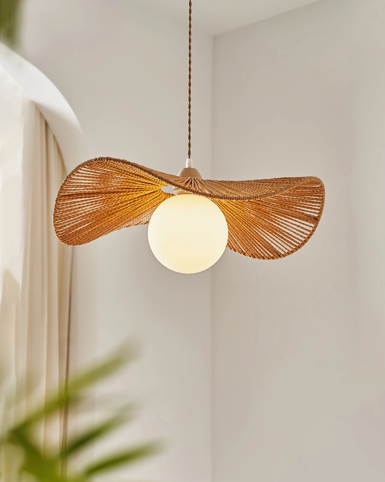 Lit Emmi rope pendant lamp with white globe bulb in minimalist corner with natural foliage backdrop