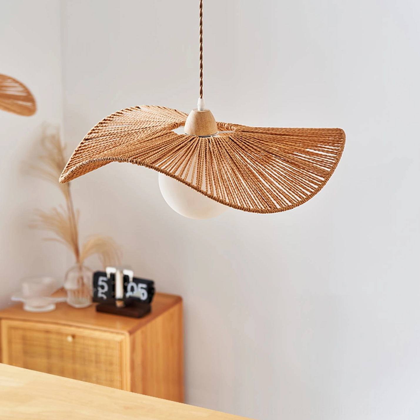 Emmi rope pendant lamp in side view position with matching wooden rattan furniture and desk clock
