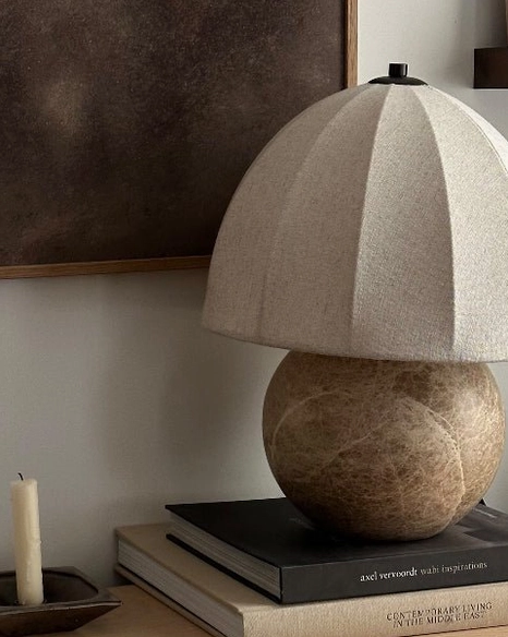 Enora table lamp with matte black finial on pleated shade, low frontal view on stacked books, rustic minimalist style