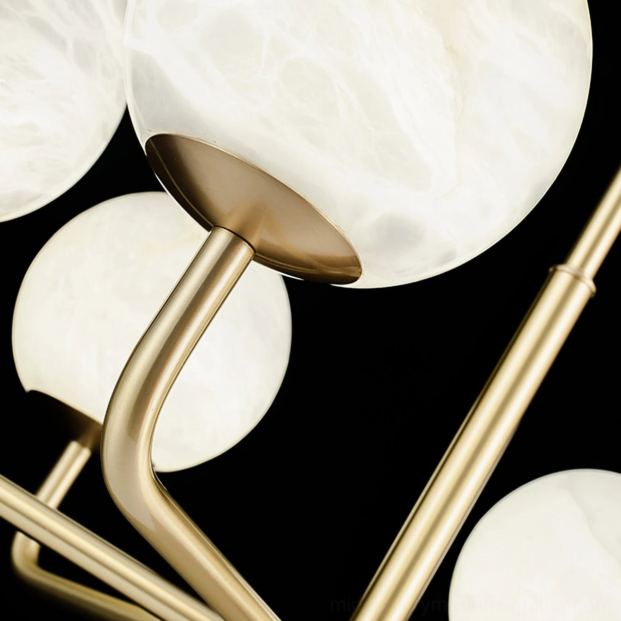 Close-up macro view of Erich chandelier showing polished brass metal arms and frosted alabaster glass globe shades