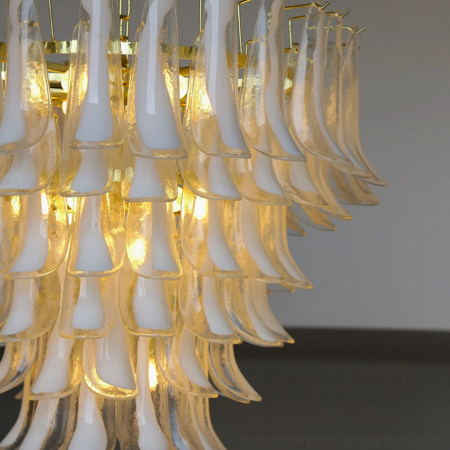 Frontal close-up of petal chandelier showcasing bright warm bulb illumination through layered frosted and clear glass petals with gold accents