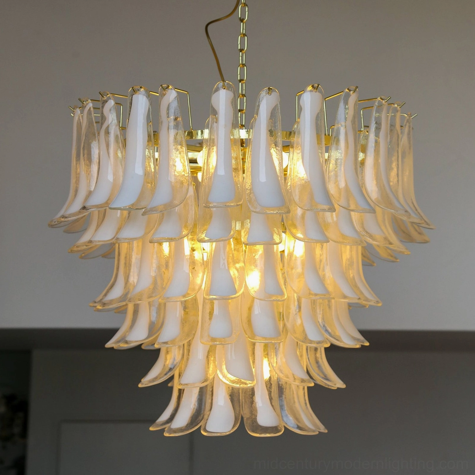 Hand-blown glass petal chandelier illuminated in modern residential living room creating warm ambient light and layered shadow effects