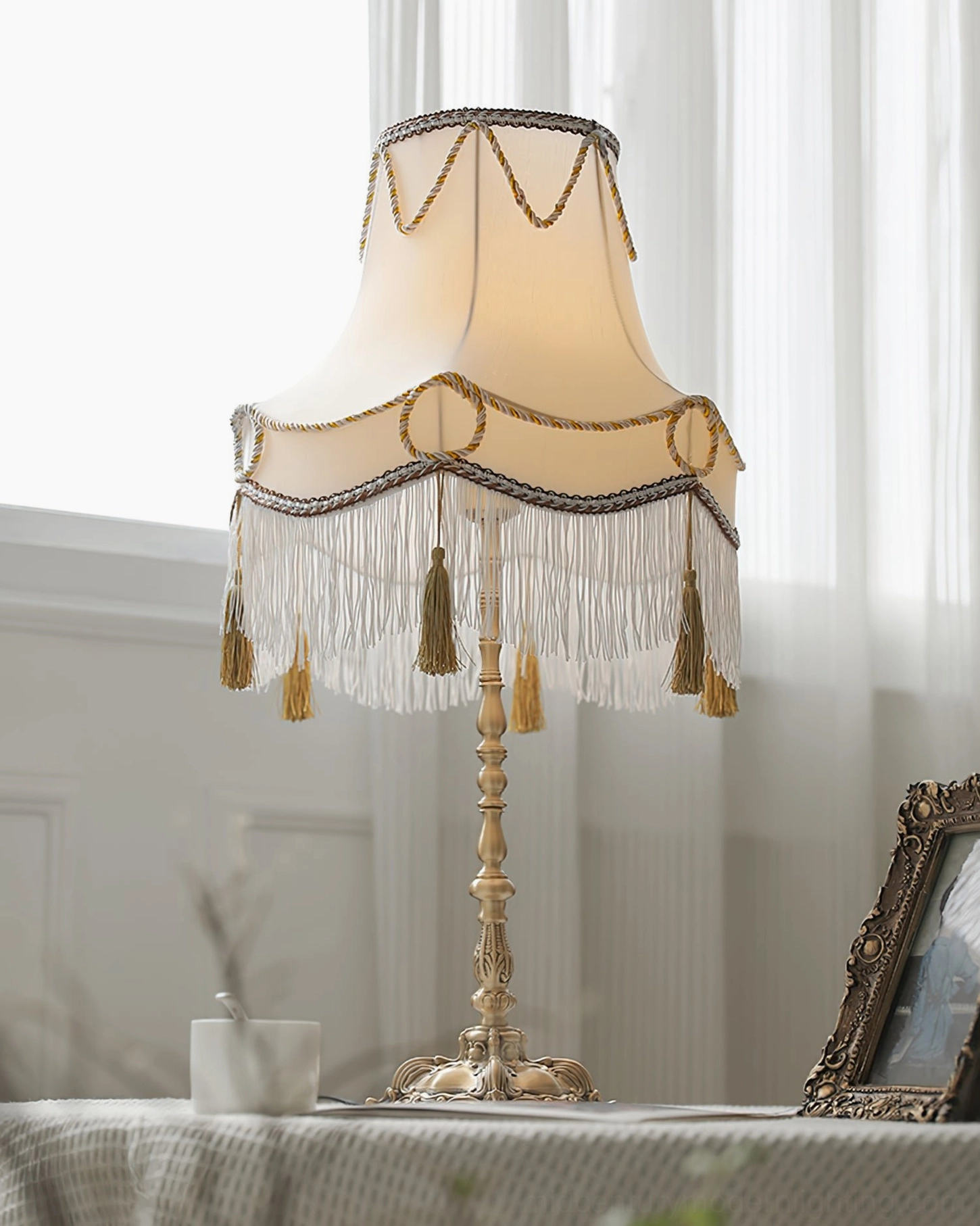 European style Victorian brass table lamp with tassel fringe shade in minimalist interior setting