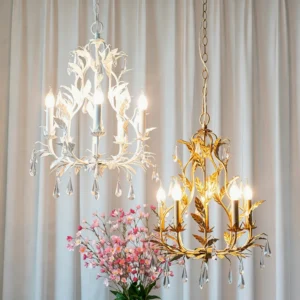 Evie Crystal Chandelier in gold and white finishes hanging side-by-side with pink floral backdrop, showcasing leaf metalwork