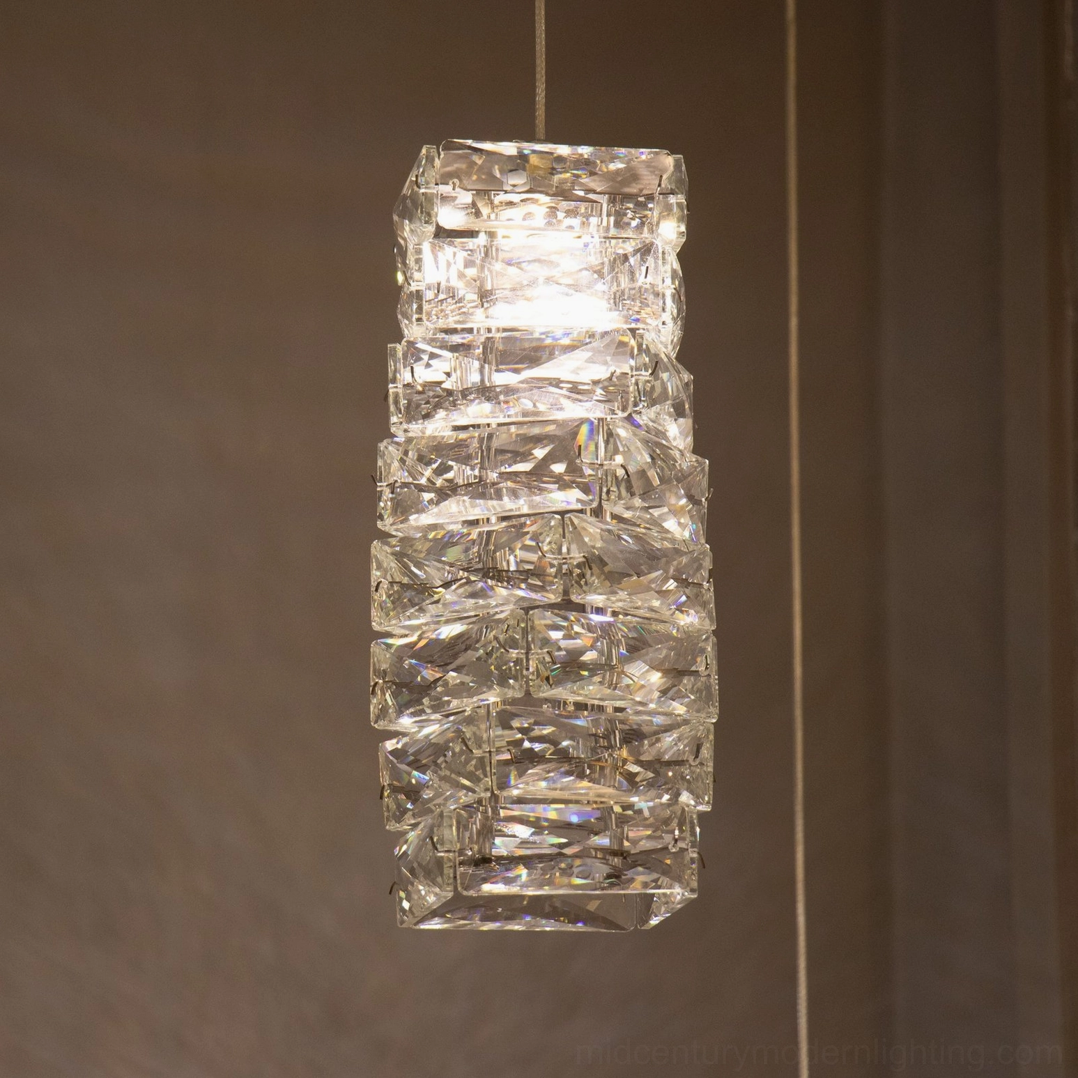 Front close-up view of thick stacked faceted clear crystal pendant lamp with bright glowing integrated LED light