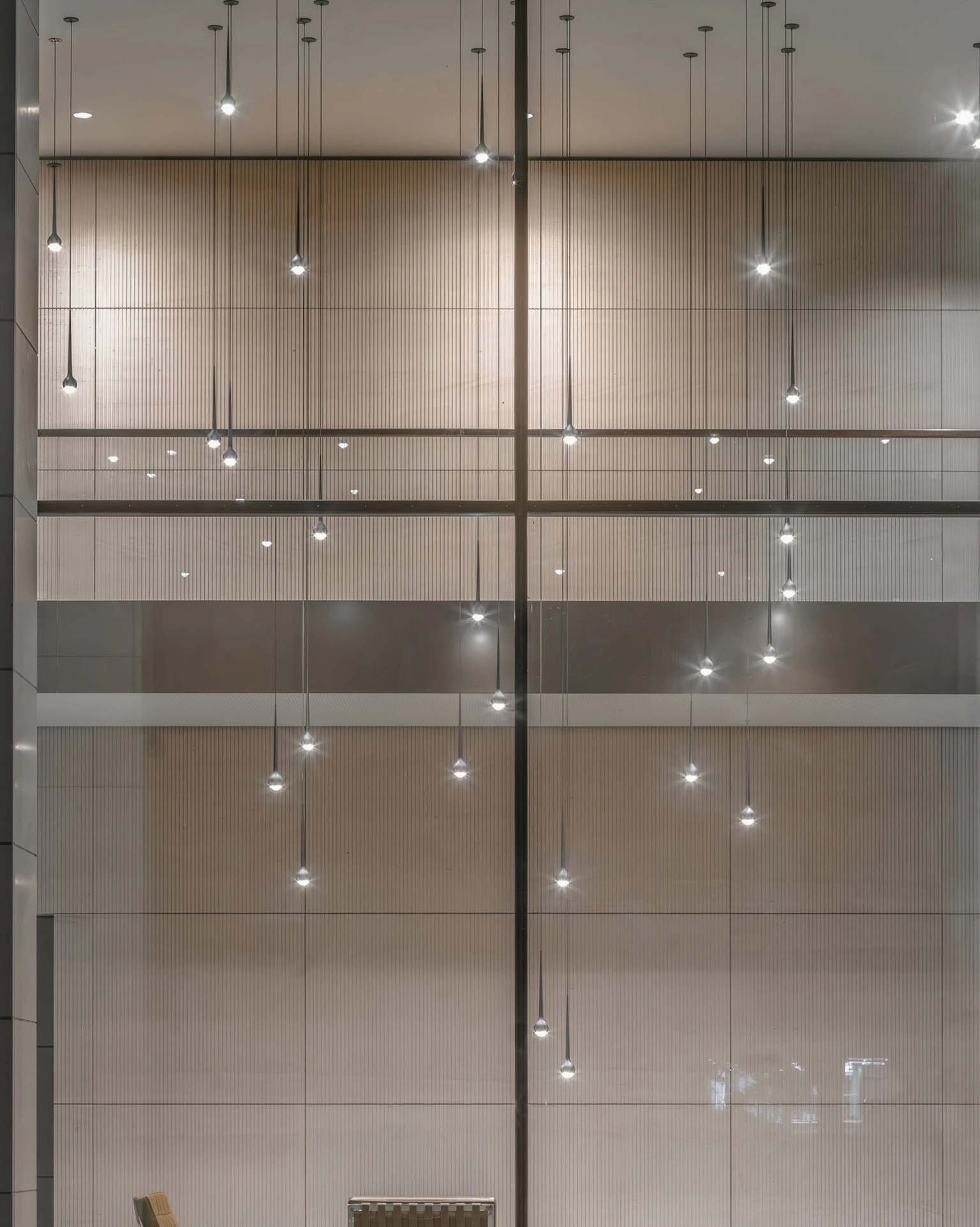 Cluster of multiple black teardrop pendant lights suspended in double-height modern lobby space
