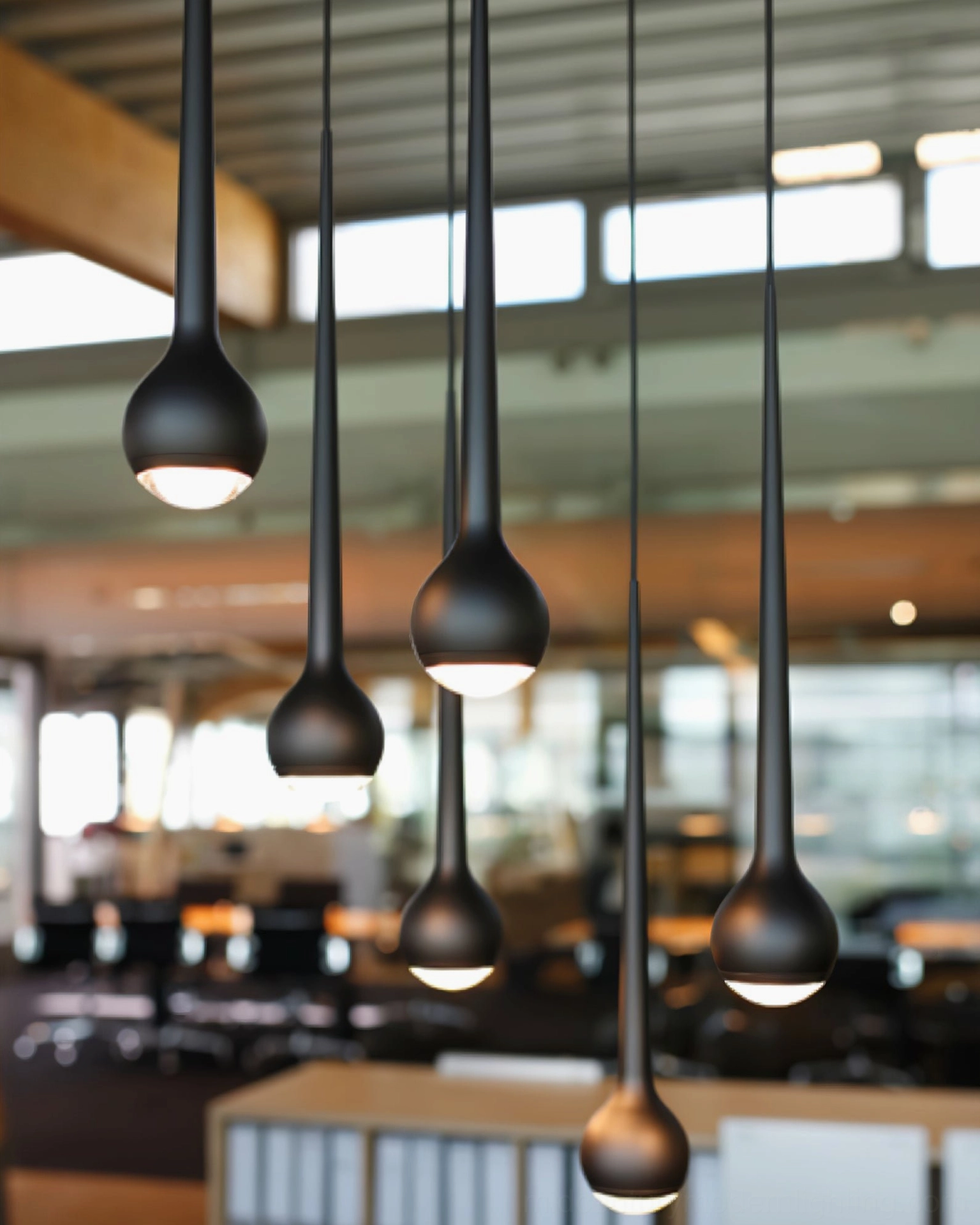 Multiple black teardrop pendant fixtures in neat row over open-plan modern office workspace