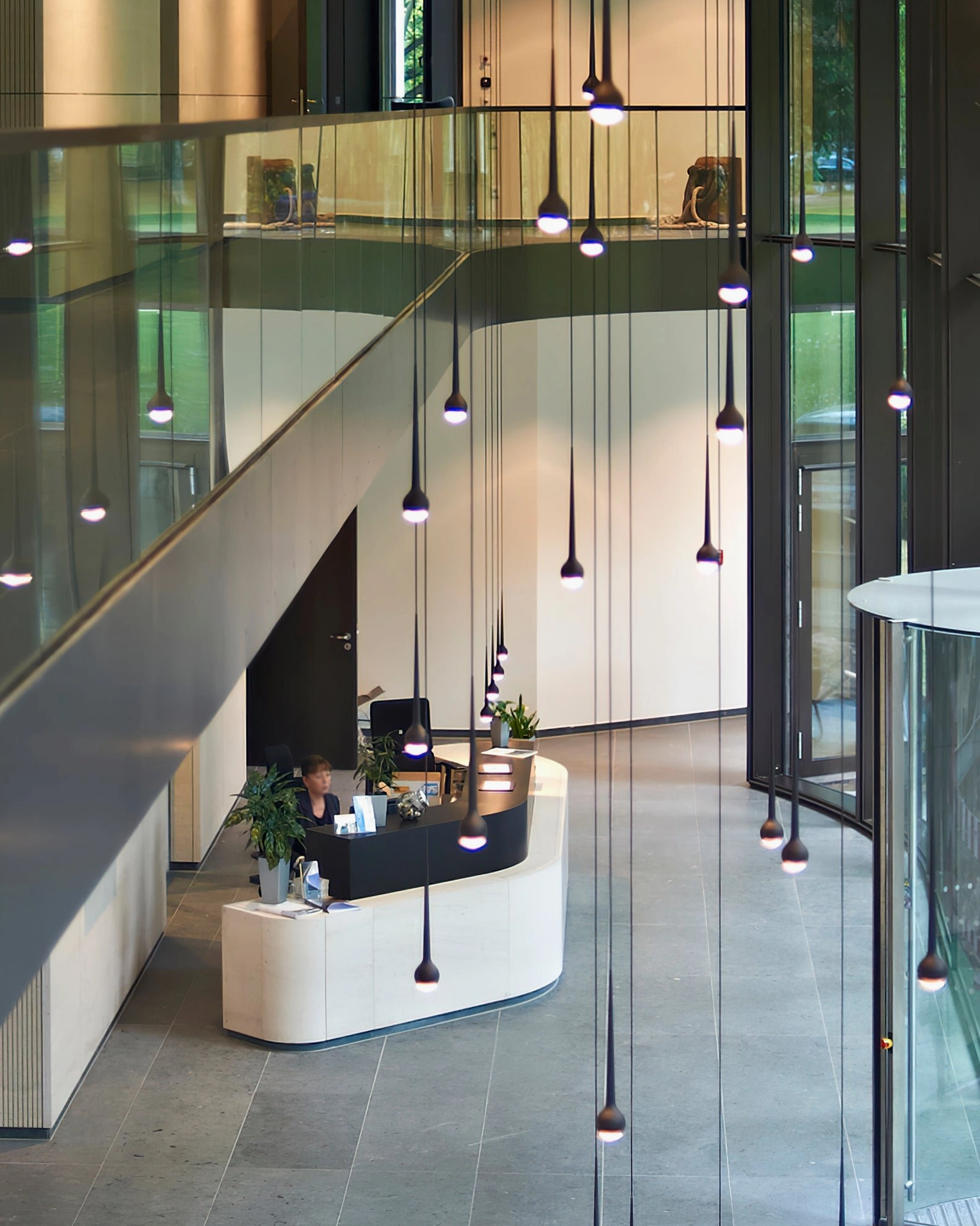 Black teardrop pendant fixtures arranged in modern office hallway with glass railings