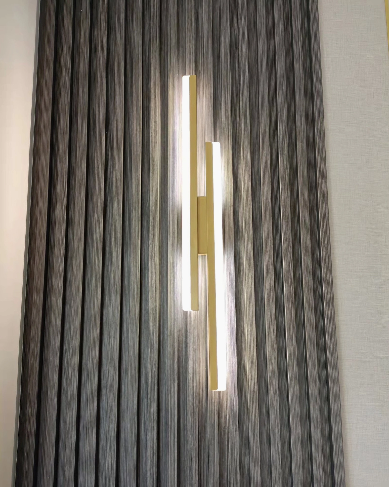 Gold Fallon sconce showcasing minimalist design against striped accent wall in modern interior