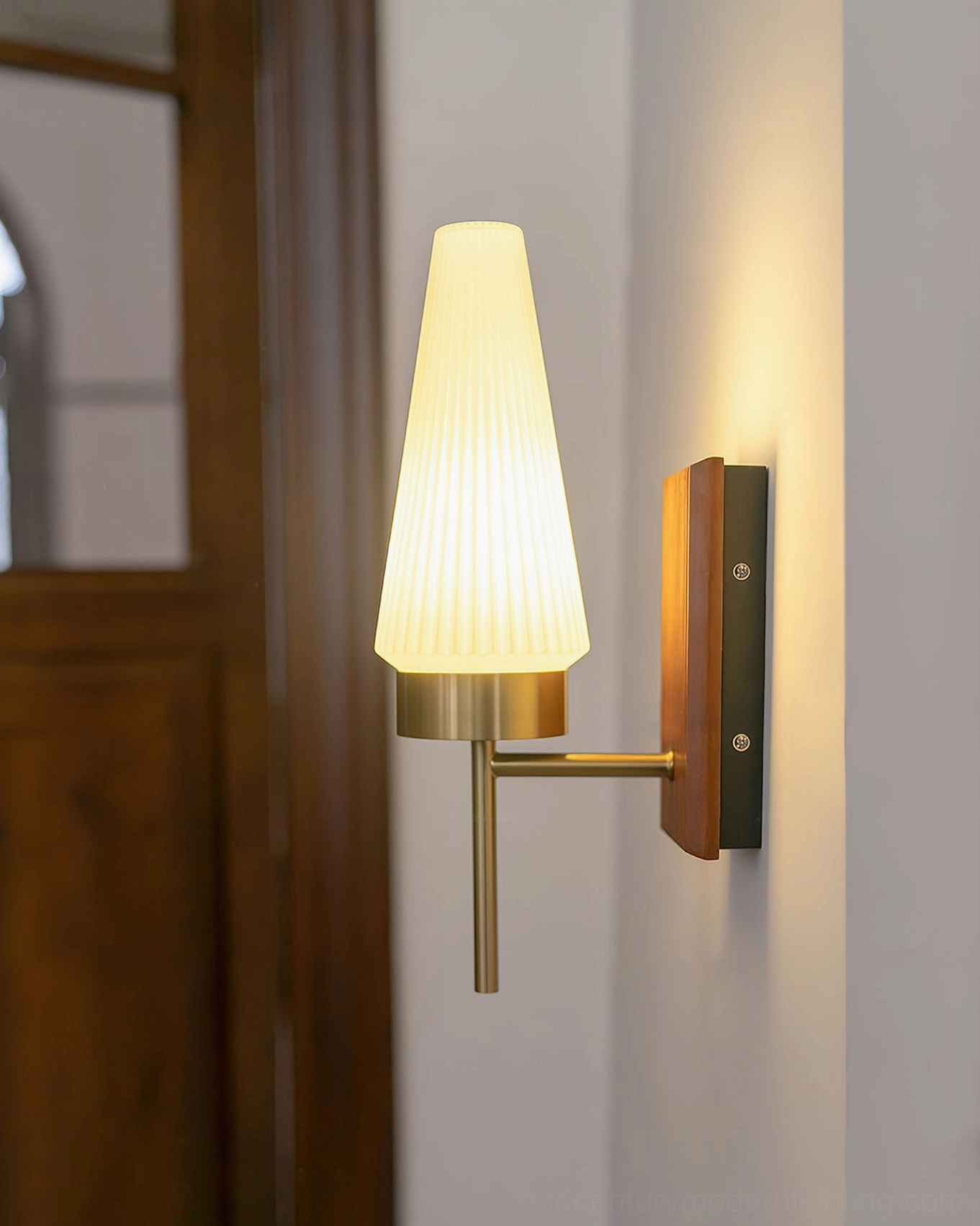 Lit Farrell wall sconce three-quarter view showing warm yellow light and wood backplate in entry setting