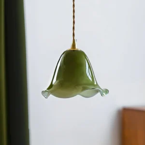 Low-angle close-up of Fazzo pendant lamp showing twisted fabric cord and brass mount detail against minimalist wall