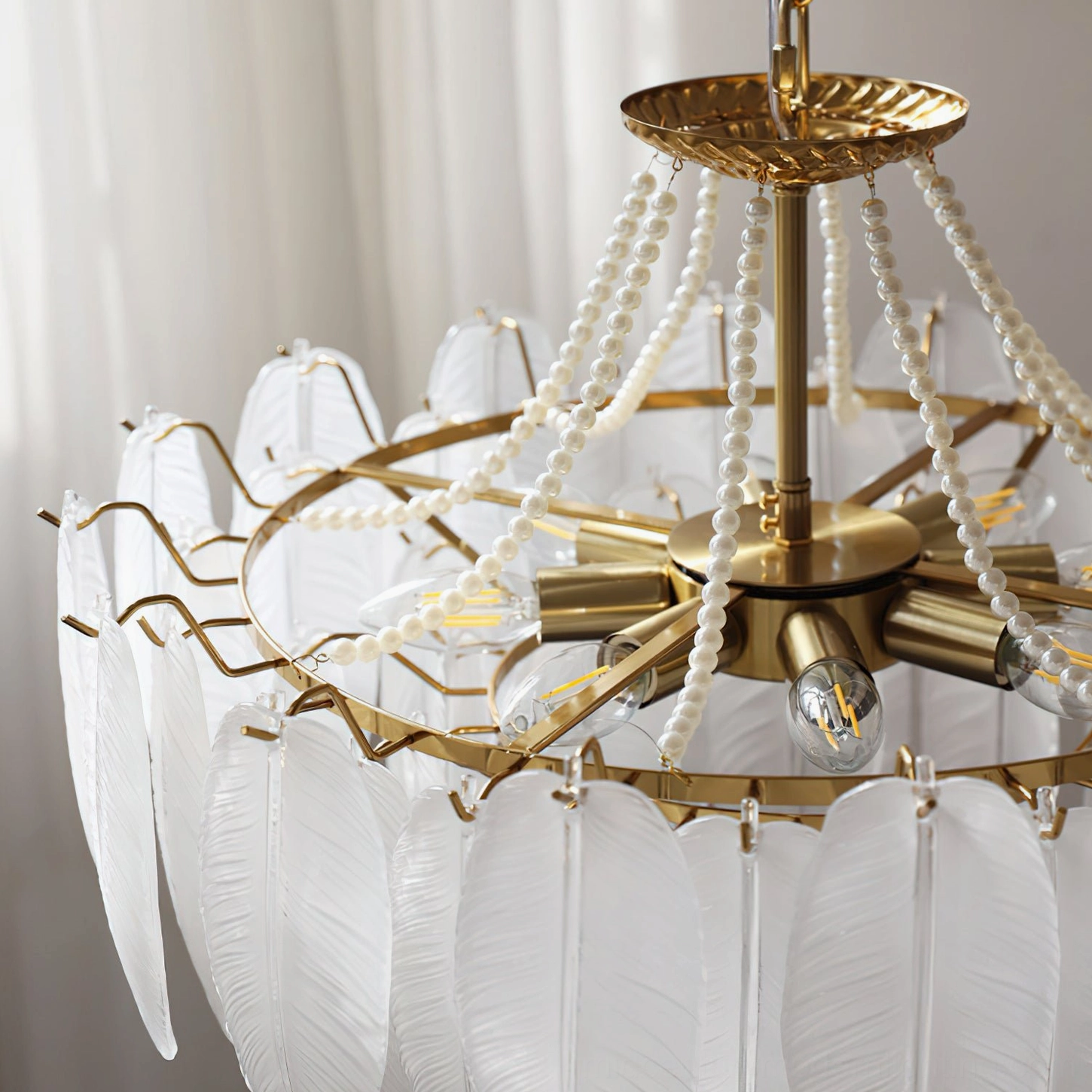 Gold finish feathered glass chandelier highlighting brass frame hardware and decorative beaded suspension chain details