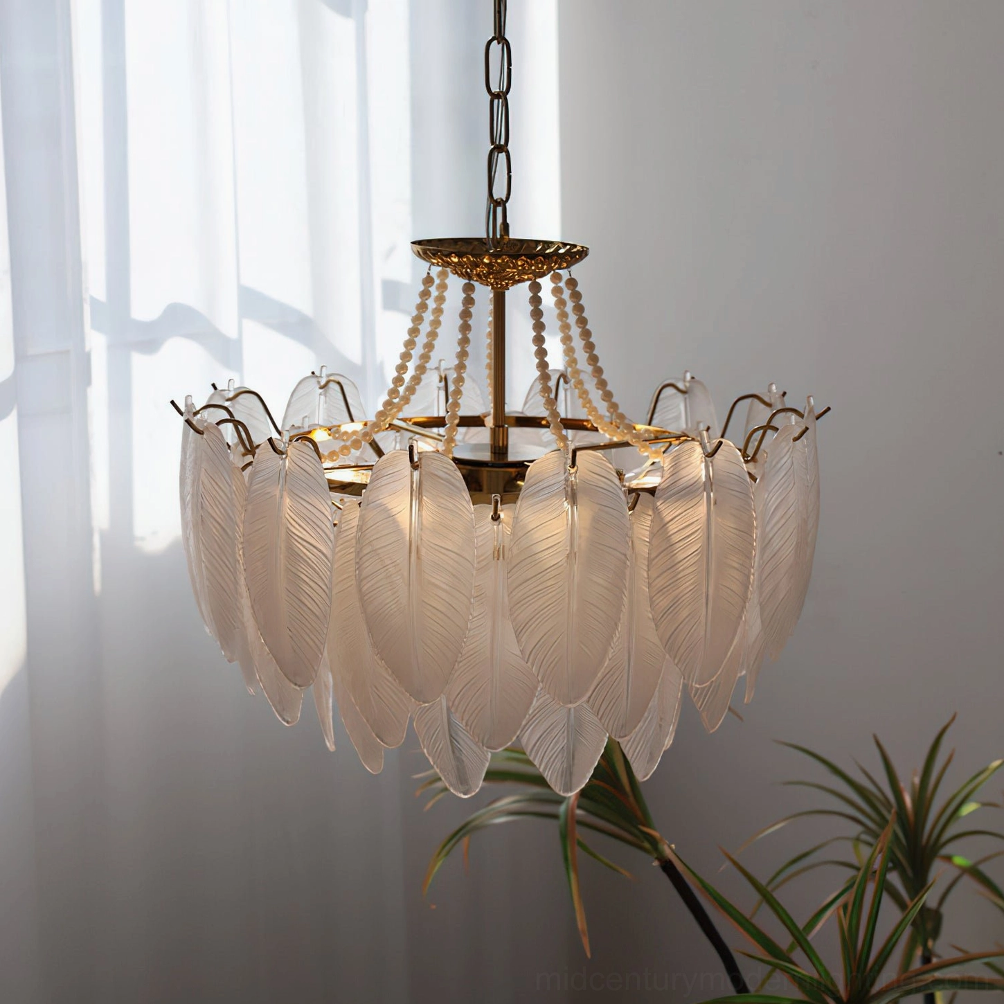 Modern feathered glass chandelier in sunlit home interior showing brass hardware and curved metal lamp holders with potted plants and sheer window treatments