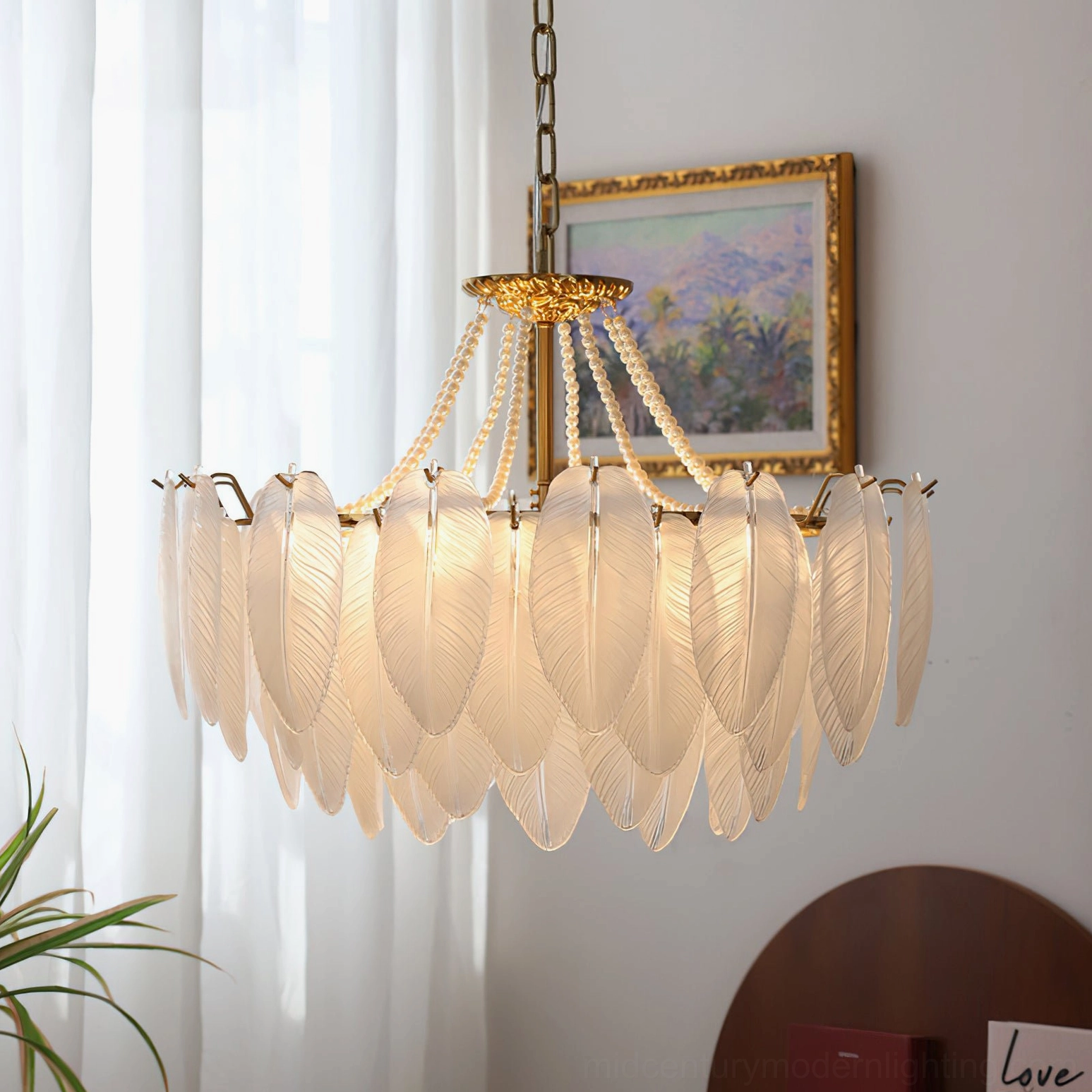 Feathered glass chandelier low frontal view in vintage living room setting with warm brown-toned glass shades, sheer curtains, framed painting, and round wooden decor