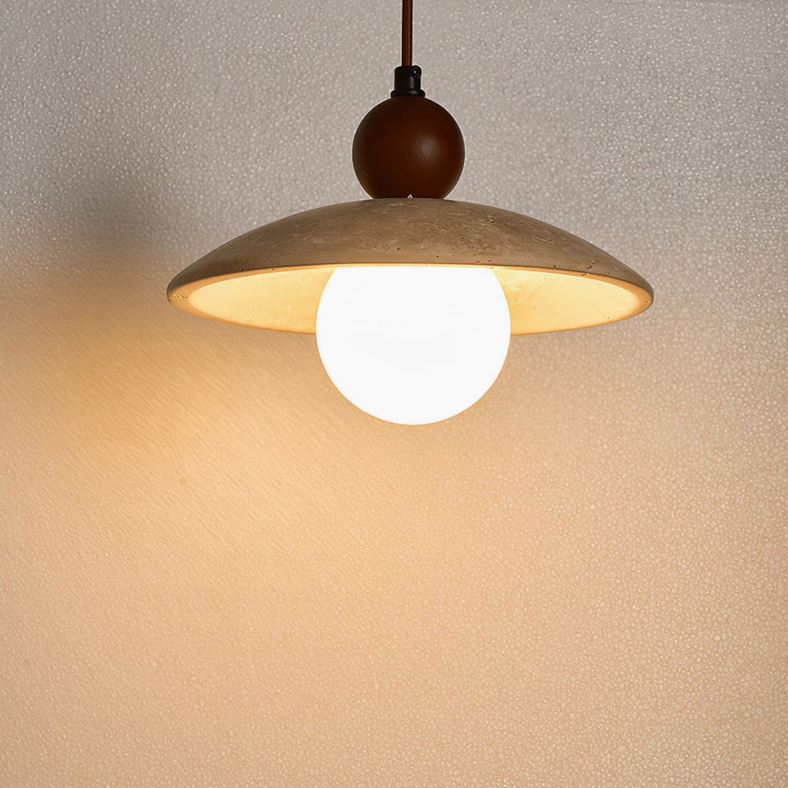 Detailed close-up of Ferox pendant showing frosted opal globe, warm lighting glow, and textured beige travertine shade