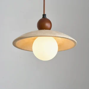 Close-up front view of Ferox pendant light with glowing frosted bulb and porous travertine stone texture