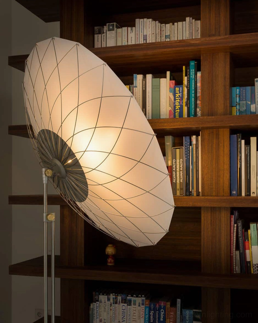 Low perspective view of filigree floor lamp showing illuminated shade with exposed wire-frame structure casting shadows