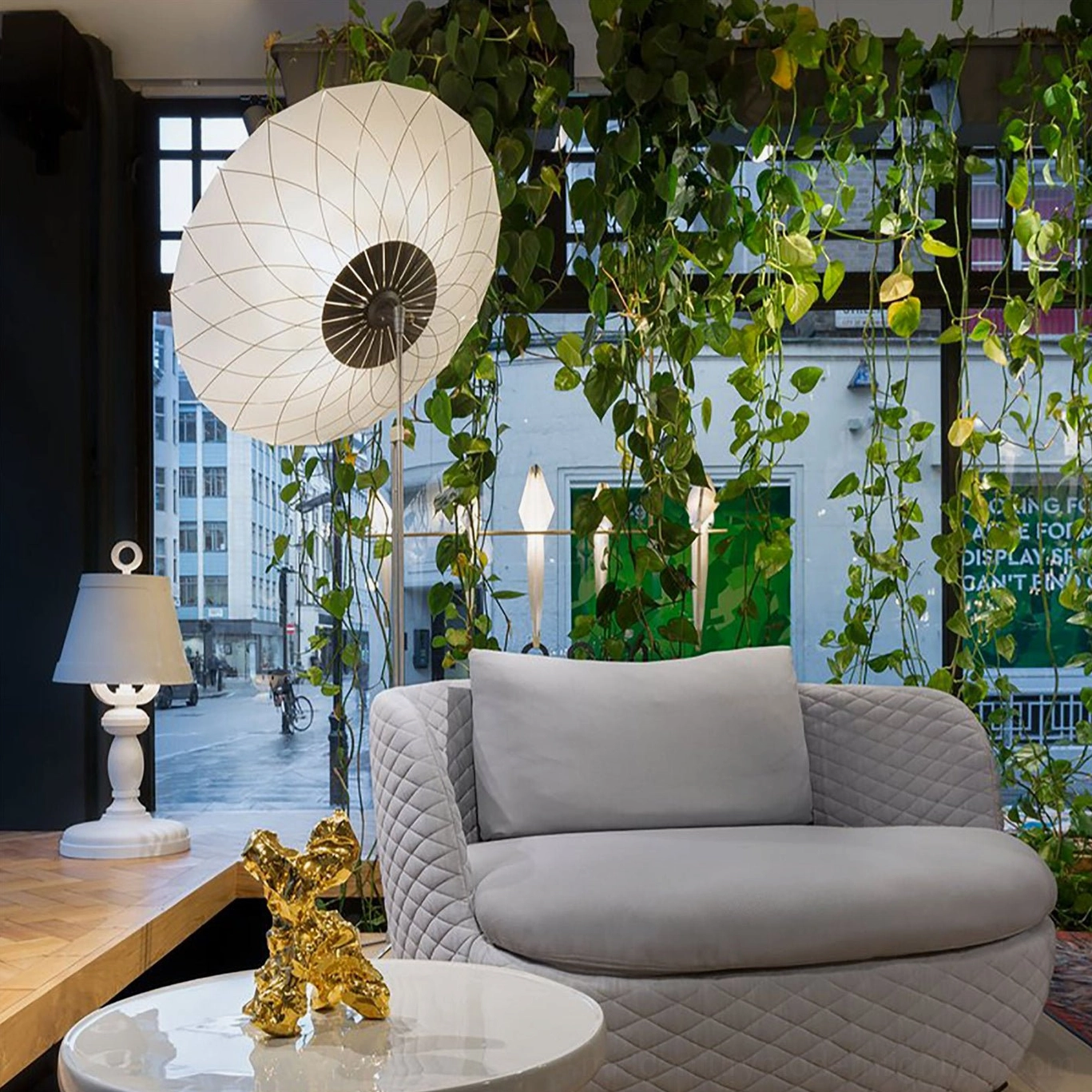 Contemporary filigree floor lamp in bright sunlit interior with large windows and green trailing plants