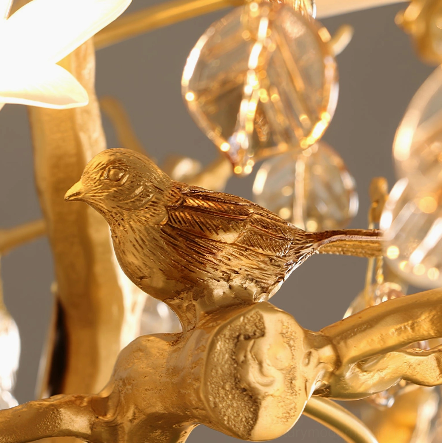 Close-up macro detail of brass bird figurine and crystal leaf on Fiori chandelier