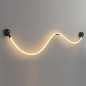 Illuminated Flecto Tube wall lamp with warm LED glow mounted on grey textured wall, close-up view of braided silicone rope and brushed black fixtures