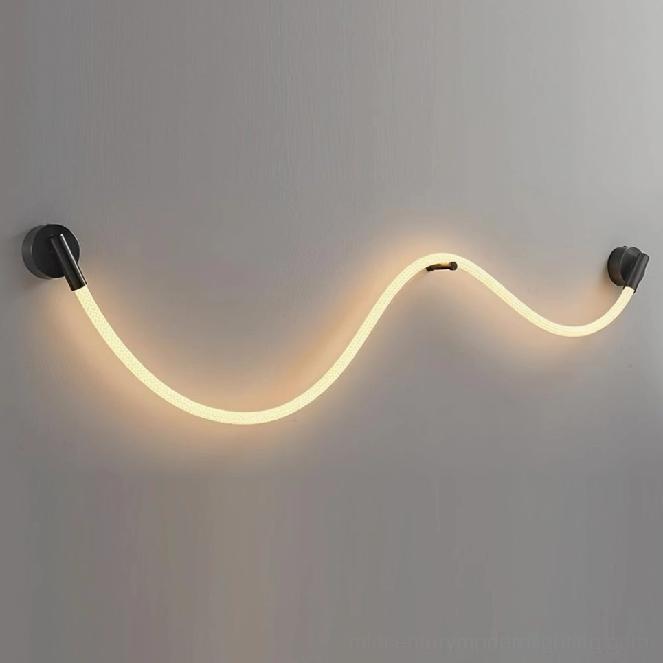 Illuminated Flecto Tube wall lamp with warm LED glow mounted on grey textured wall, close-up view of braided silicone rope and brushed black fixtures